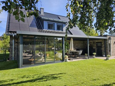 Moderner Wintergarten mit Flachdach und Glasschiebetüren an einem Einfamilienhaus mit Klinkerfassade