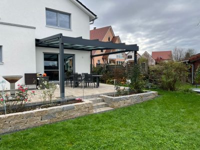 Moderne, anthrazitfarbene Aluminium-Terrassenüberdachung mit Glaselementen an einem Einfamilienhaus