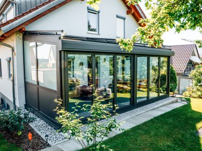 Moderner, freistehender Wintergarten in Anthrazit mit Glasschiebeelementen an einem Einfamilienhaus
